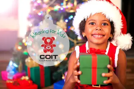 COIT Kleaning for Kids logo with young girl sitting in front of a Christmas tree holding a wrapped present looking at the camera.