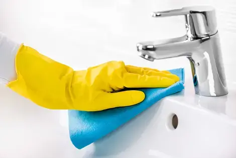 Yellow Latex Gloved Hand Cleaning a Sink and Faucet with Disinfectant 