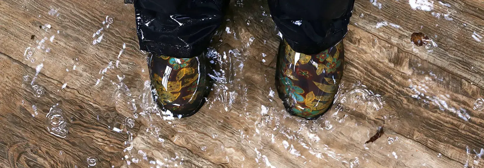 Person in boots stands on a wood floor covered in water.