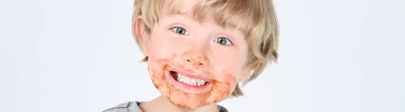 Young child holding unwrapped chocolate bar looking at camera with chocolate residue around mouth.
