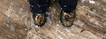 Person in boots stands on a wood floor covered in water.